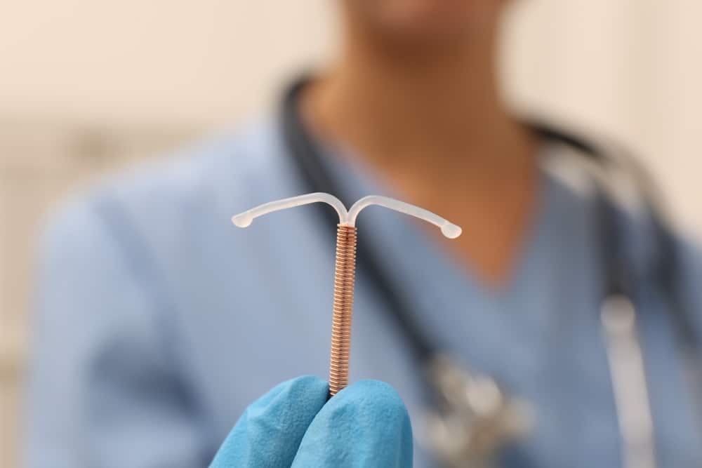 Medical professional wearing blue gloves holding a copper Paragard IUD, illustrating defective device litigation.