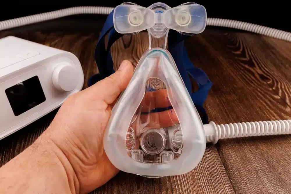 A white CPAP machine with its display and mask is displayed on a dark wooden table