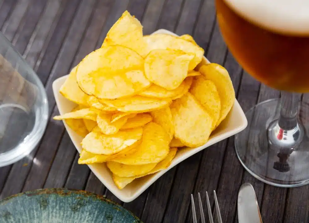Crispy potato chips with glass of cold beer served on table.